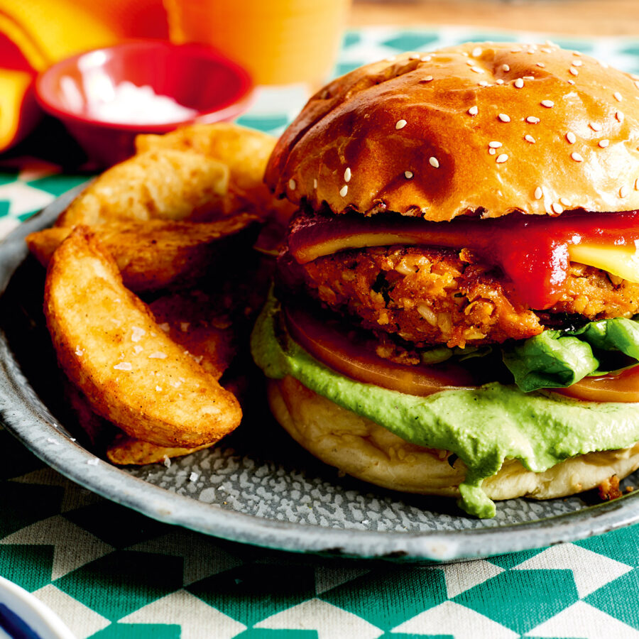 A plate with a veggie burger topped with lettuce, tomato, plant-based cheese, onion, and tomato sauce, served with thick potato chips.