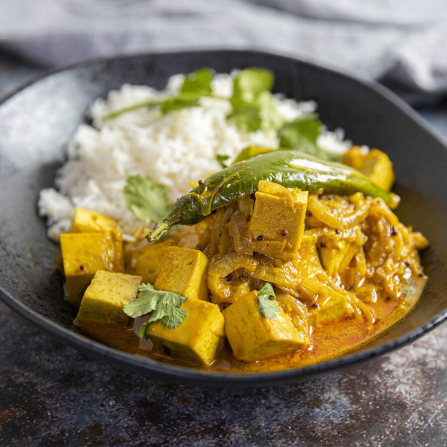 Delicious looking tofu masala curry with rice on side in a bowl