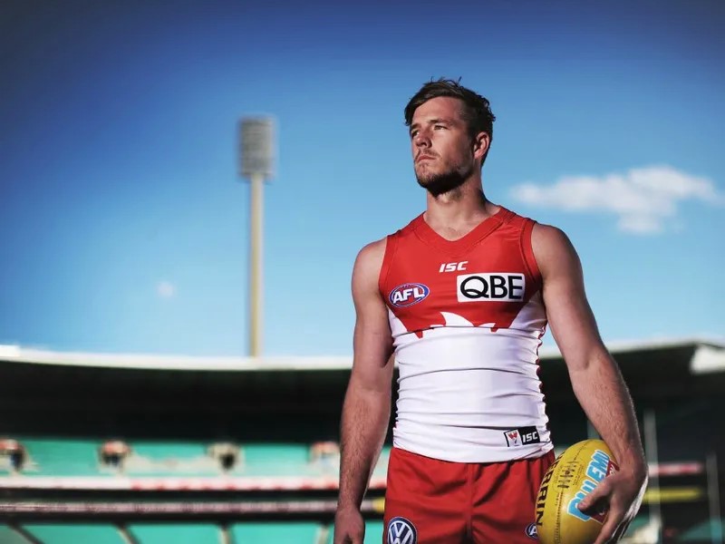 Luke Parker stands in the middle of the SCG in his Sydney Swans guernsey, holding a football.