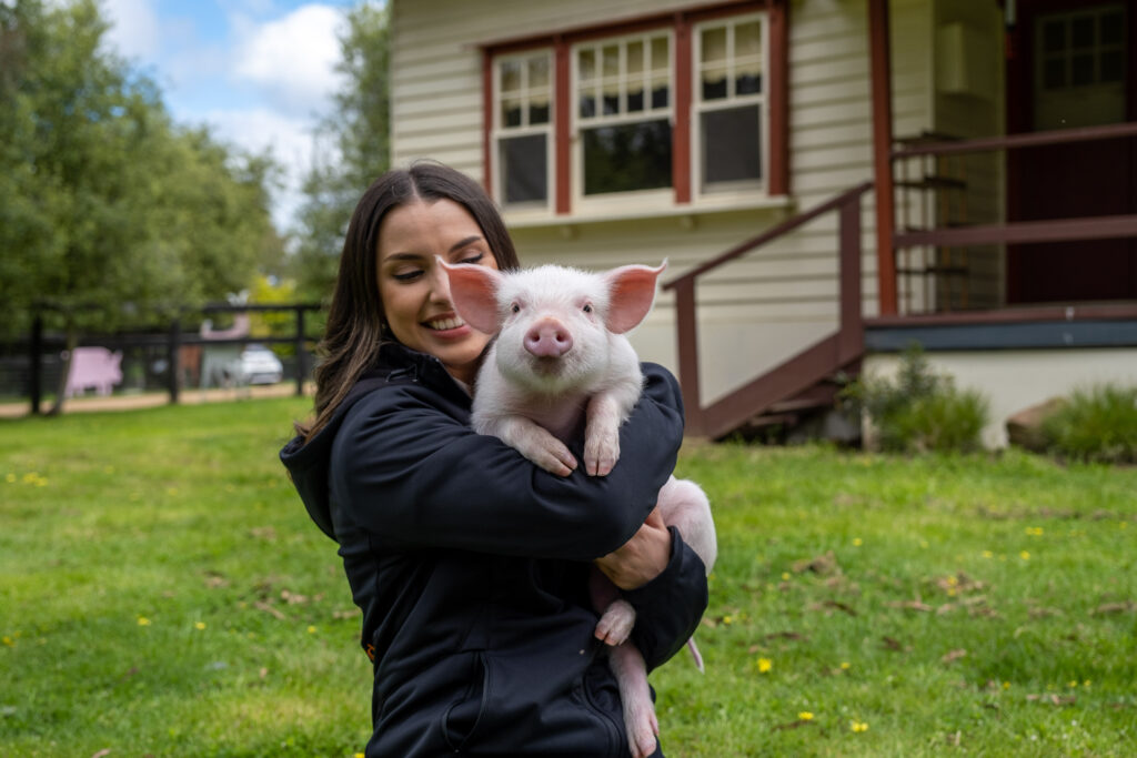 Smiling woman holds an adorable piglet, advocating for plant-based eating